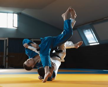 Two young fighters in kimono training martial arts in the gym. Concept of healthy lifestyle, sport, action, motion and movement. Two caucasian man practicing in white and blue kimono.